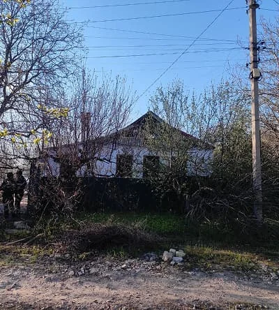 The house on Ukrainska Street after the occupation: bare trees, a dark fence, two people by the gate