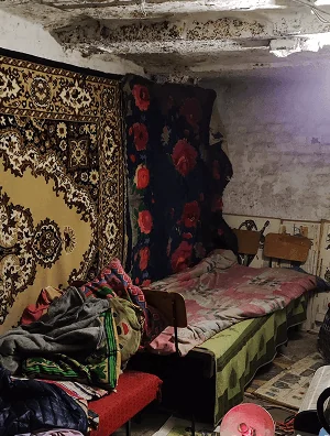 The cellar, carpets hung on its walls, a bed made up under them