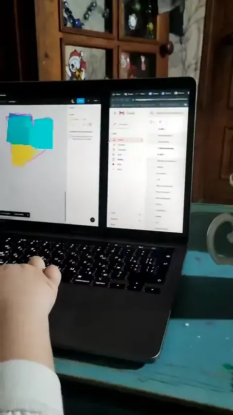 A frame from a video: a laptop open on a table in the house, a child's hand at the edge of the frame.